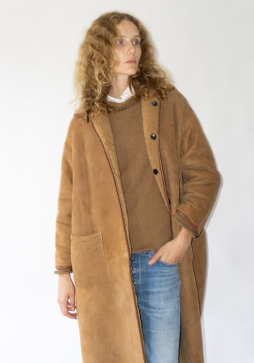 Woman wearing a long brown coat over a sweater and jeans on a white background