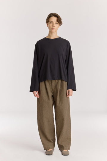 Person wearing a black long-sleeve top and beige pants on a white background