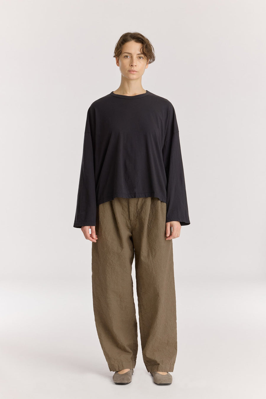 Person wearing a black long-sleeve top and beige pants on a white background